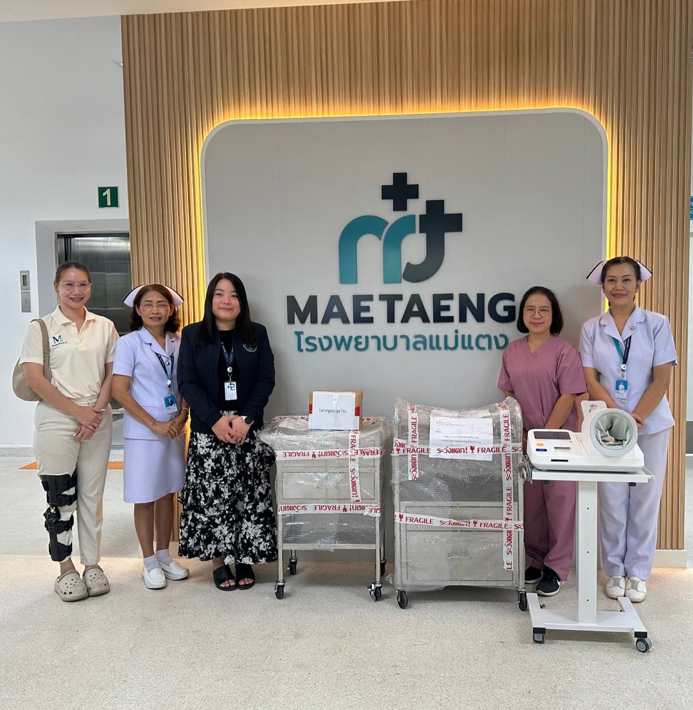 Nursing staff at Mae Taeng Hospital with the delivered emergency trolley, dressing trolley, laryngoscope set and automatic blood pressure monitor.