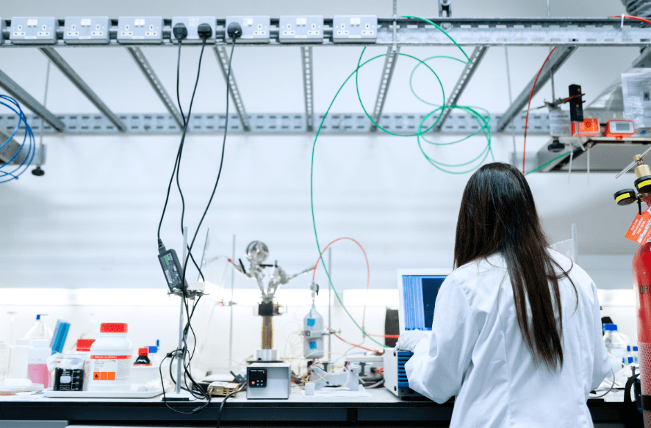 A laboratory bench with glassware, instruments and tubing, and an analyst working at the far end